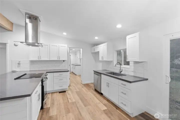 A clear look at the updated kitchen featuring white shaker cabinetry, subway tile backsplash, and sleek solid-surface counters. The wide layout provides generous prep space, excellent storage, and room for multiple cooks. Bright recessed lighting and the window above the sink keep the space feeling open and fresh.