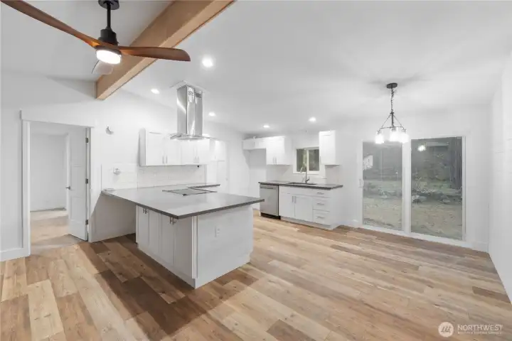 An open view of the kitchen and dining space, showing how the layout flows naturally toward the sliding doors and outdoor area. The island offers additional seating and workspace, while the warm wood flooring ties the entire great-room area together. This angle helps buyers visualize the home’s flexible everyday living and entertaining potential.