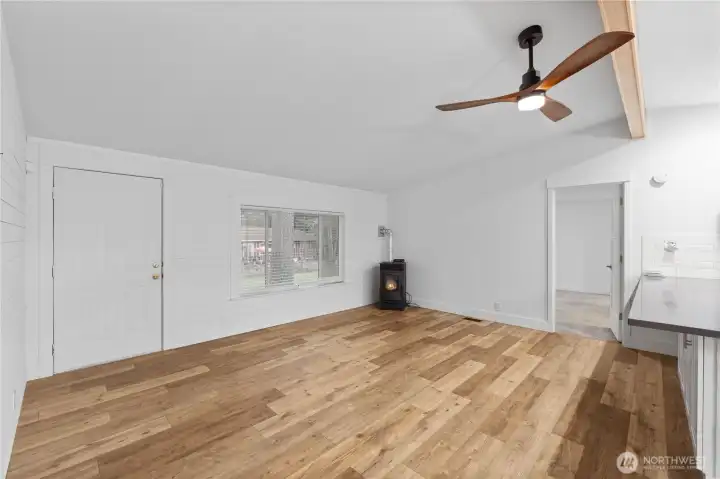 Another angle of the living room showing the open layout, large front window, and the wood-burning stove that warms the space. This view highlights how the room connects with the kitchen and hallway, giving buyers a better sense of the home’s flow and usable space.