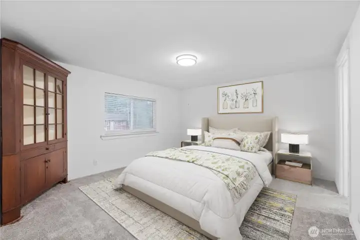 The staged primary bedroom highlights the room’s generous size and calming color palette. Soft carpeting, wide wall space for larger furniture pieces, and a centered window for natural light create an inviting retreat. The staging showcases how comfortably the room can accommodate a full bedroom set.
