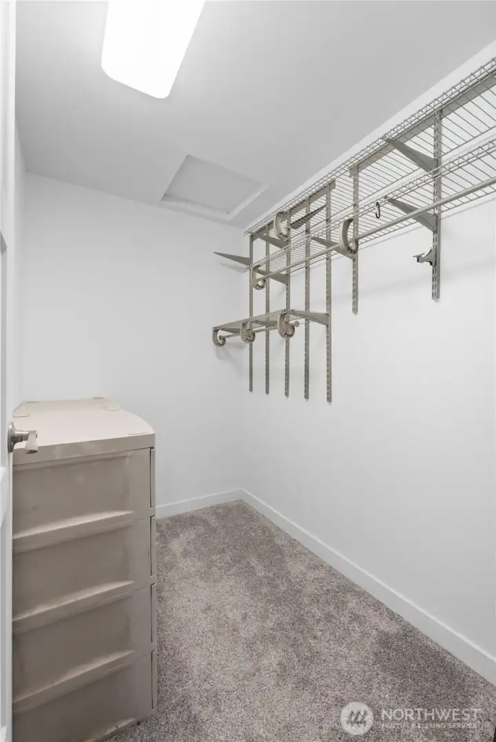 This walk-in master closet offers efficient storage with built-in wire shelving and multiple hanging sections ready for organization. Fresh carpet and bright lighting give the space an open feel, and the simple layout makes it easy to visualize how wardrobes, bins, or additional shelving can be arranged.