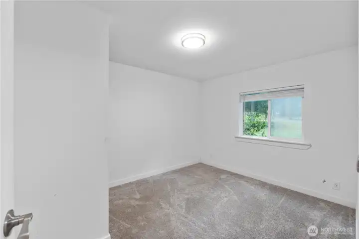 This secondary bedroom includes soft carpeting, a large window for natural light, and a simple layout that works well for a guest room, office, or nursery. Neutral paint and clean lines make it easy for buyers to imagine their own setup here.