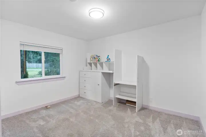 A spacious third bedroom with plush carpeting, a large window overlooking the yard, and plenty of room to configure a desk, bed, or storage. Simple lines and neutral walls make it easy to tailor the space to any use, from a hobby room to a comfortable bedroom.