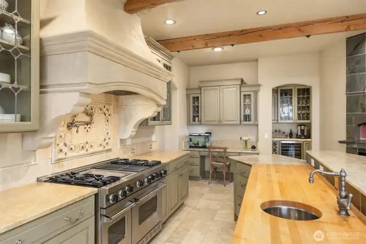 Viking Double Range with commercial vent-a-hood housed in a beautiful Limestone chimney. Marble and butcher block counters team up with the stainless prep sink. Pot filler over the stove.