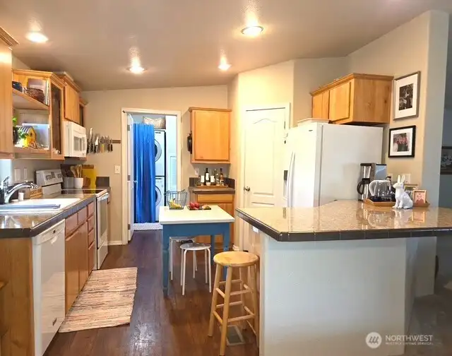 Light-filled kitchen with laminated floors and newer appliances flows into dining and living room. The utility room connects directly to the kitchen and the back door, enhancing the home’s overall flow and functionality.