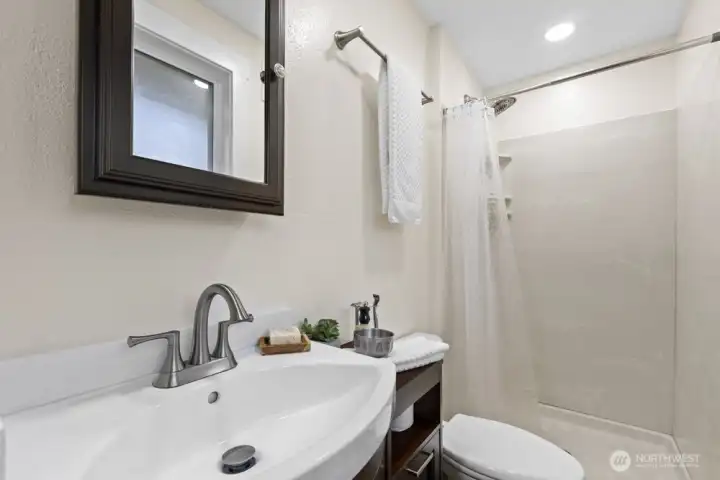 The updated primary bath makes good use of the space with added storage and a shower. Obscure glass adds privacy.