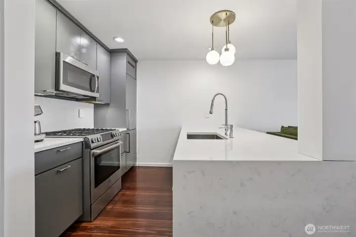 A chic chef's kitchen greets you with a waterfall quartz bar, high-end stainless steel appliances, and sleek cabinets.
