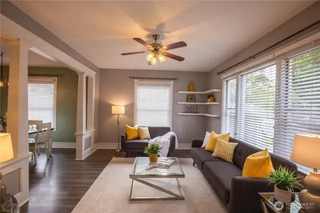 The living room is light and bright with tall ceilings, corner shelving and ceiling fan, with beautiful easy care updated LVP flooring and white trim throughout the home .
