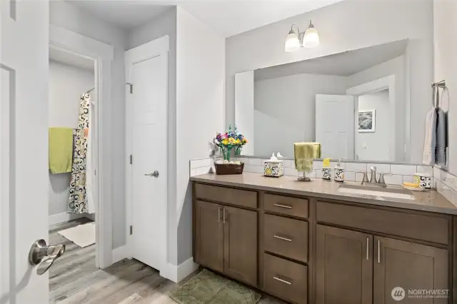 Shared bathroom with quartz counters, extra storage space in linen closet, and bath/shower combo in separated room.