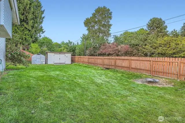 Side yard has firepit area, a shed, greenhouse and fencing.