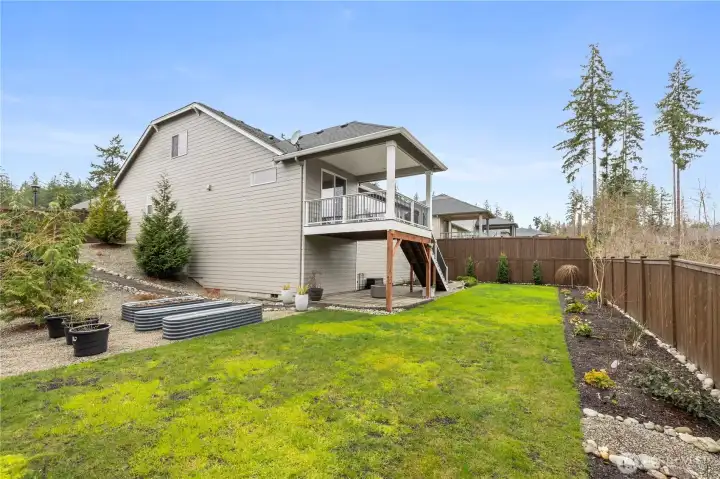 Fully fenced backyard with usable lawn space, landscaped borders, and a covered deck for easy outdoor living