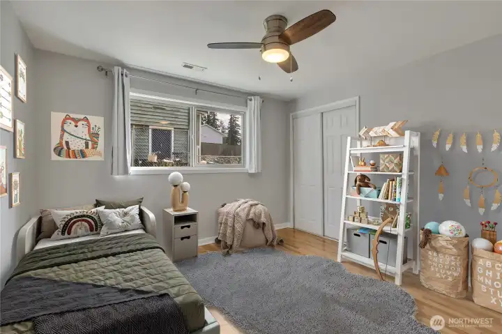 Light and bright bedroom with hardwood floors, large window and ceiling fan.  Photo is virtually staged.