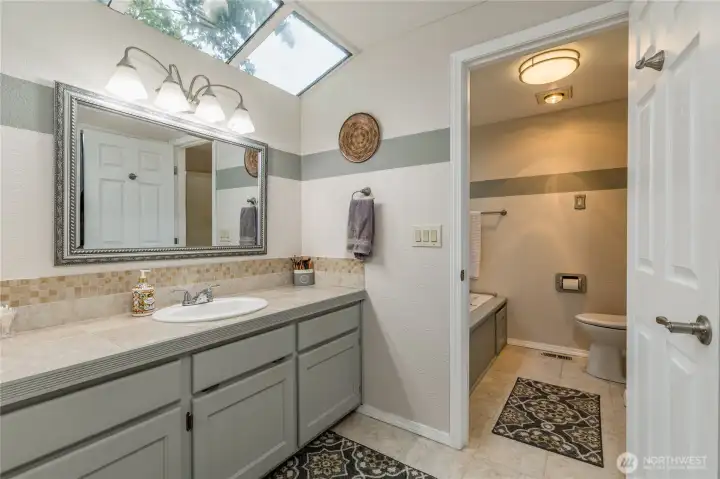 A view of the primary bath vanity and skylights, with the separated area for the toilet and jetted tub A view of the primary bath vanity and skylights, with the separated area for the toilet and jetted tub
