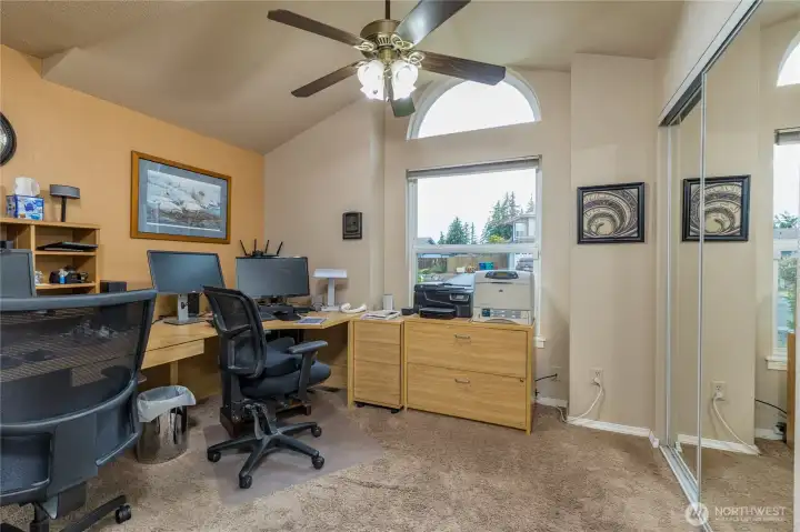 A bedroom with a vaulted ceiling, carpeting, and a window fanlight, in addition to the combination fan/light, currently being used as an office A bedroom with a vaulted ceiling, carpeting, and a window fanlight, in addition to the combination fan/light, currently being used as an office