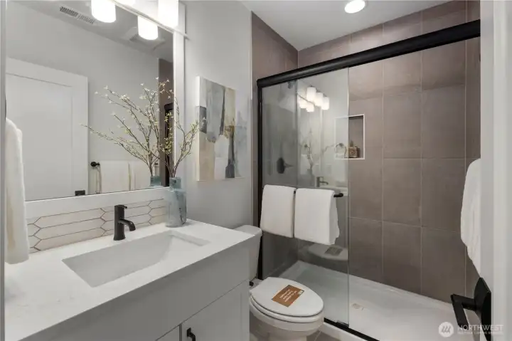 Main Floor Bath: Stylish full bath features modern tile, quartz counters, and a glass-enclosed shower. Conveniently located near the main-level den or guest bedroom for added privacy and comfort.    Photos are from THIS model home at Foxmoore but are for visualization purposes only.  Photos are from the model home at Foxmoore and for visualization purposes only. Plans, colors, building orientation, finishes, home outlook, and other details can and WILL vary.