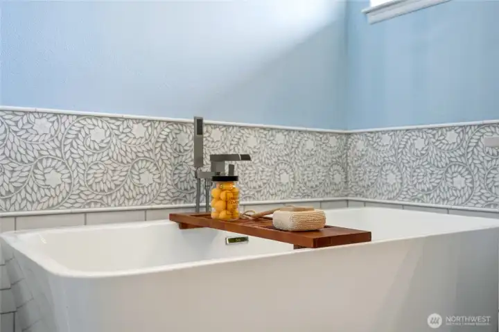 Elegant freestanding soaking tub in the upstairs primary bath, accented by decorative tile surround and modern fixtures for a spa like retreat.