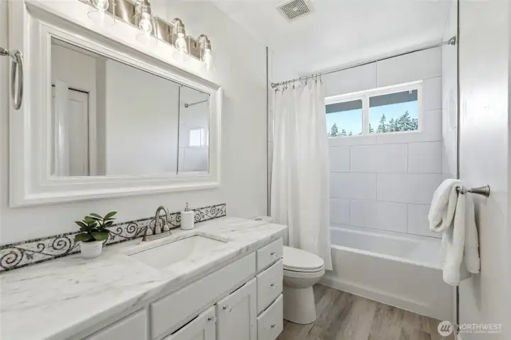 Beautifully remodeled second floor bath featuring a marble countertop vanity, updated lighting, and a bright tiled tub and shower surround.