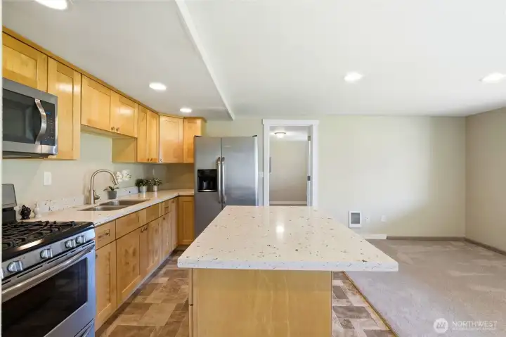 Well-equipped ADU kitchen featuring gas cooking, stainless appliances, quartz counters, and a generous island for prep and seating.