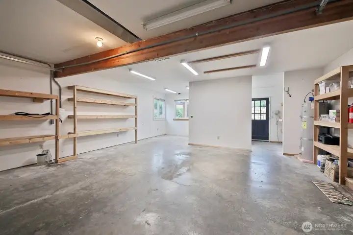 Spacious 2 Car Garage with plenty of built-in storage and an EV Charger. The hot water heater is located here and there is additional space beyond the partial wall straight ahead. The door to the house is along the right edge of the photo.