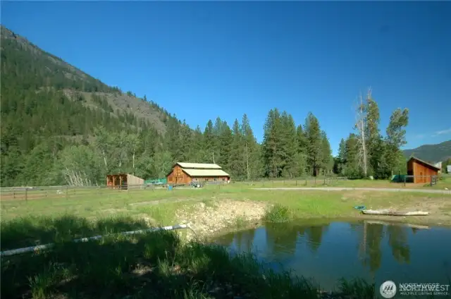 Peaceful pond framed by barn, forest, and mountains—wildlife haven and serene backdrop for ranch life