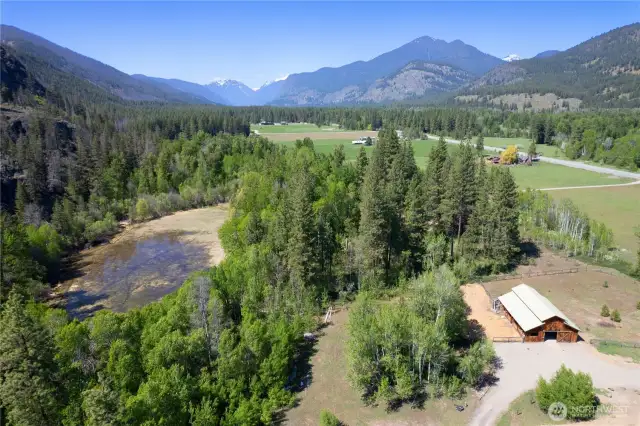 Expansive aerial showcasing lush forest edge, open meadow, pond, and mountain panorama—true Methow Valley beauty