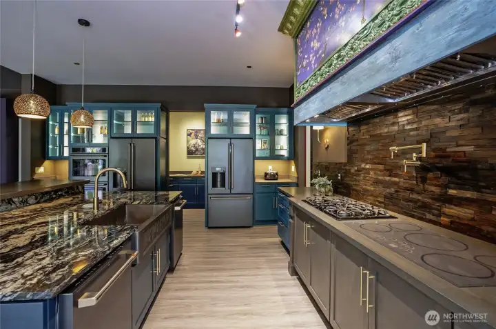 This luxury kitchen features dual 36" cooktops (gas and induction) with a convenient wall pot filler, all showcase-framed beneath a custom-artisan twin hood cover. Twin dishwashers flank the designer copper sink on each side.
