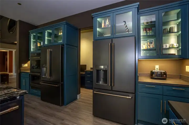 Built for elite entertaining, the space is anchored by a high-end suite of GE Café appliances in matte black—including dual refrigerators and double wall convection ovens—all beautifully framed by glass-lit display cases.