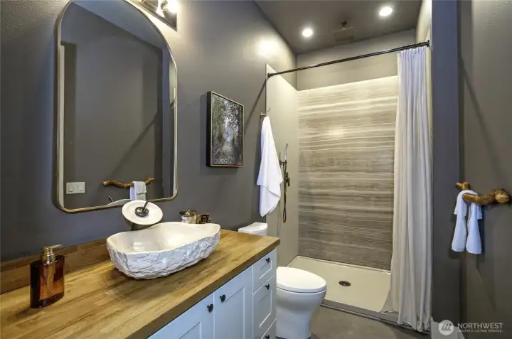 This private bathroom features a striking chiseled stone vessel sink and a sleek walk-in shower with a rainfall showerhead. The organic textures elevate the space, offering a sophisticated, design-forward retreat.