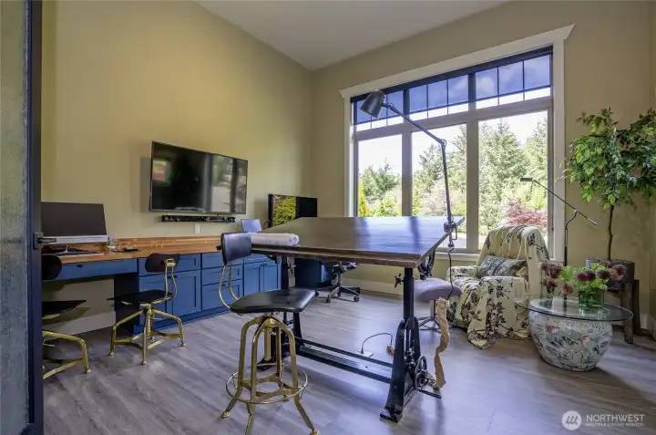 Soaring scale meets exceptional functionality in this sun-drenched home office. A massive window framing the greenery anchors a commanding footprint designed for creative projects or the ultimate remote work headquarters.