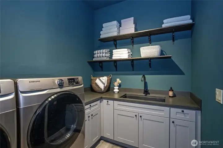 This laundry room also features an XL wall-mounted towel warmer on the opposite wall, which adds elite functionality—perfect for gently drying sensitive clothing.