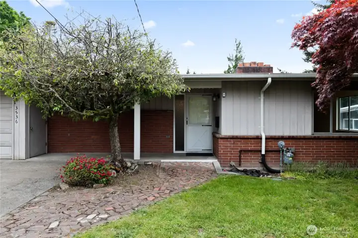 There is a covered porch, with a flagstone walkway, shaded by a tree. There is a covered porch, with a flagstone walkway, shaded by a tree.