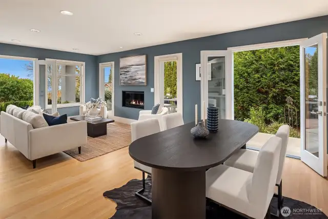 Bathed in natural light, this sophisticated living room combines stunning lake views through wraparound windows with contemporary design elements. A sleek gas fireplace, rich blue accent walls, and French doors to outdoor spaces create an ideal environment for modern living.