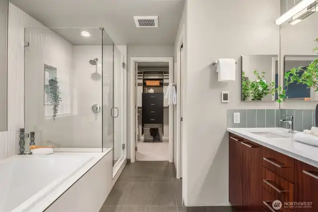 Modern primary bathroom showcases dual vanity, deep soaking tub, and seamless glass shower with designer tiles.