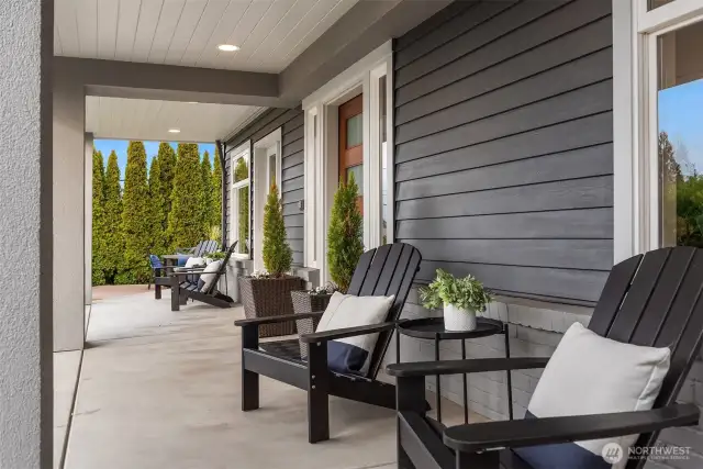 Spacious covered porch creates an inviting retreat with contemporary outdoor furnishings and elegant landscaping.