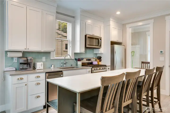 The stylish kitchen features ceiling-height cabinetry with crown molding, quartz countertops, stainless-steel appliances, and a full tile backsplash.
