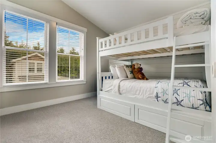 The second bedroom has sunny windows, a full-size bunk bed with storage drawers, and a vaulted ceiling that adds a light, airy feel.