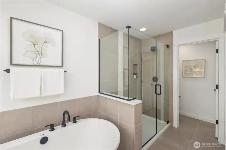 Primary Bath – Tub & Shower:  This angle highlights the pairing of a freestanding soaking tub with a spacious glass-enclosed shower, creating a balanced mix of relaxation and efficiency. The neutral tile palette adds warmth and continuity throughout the room. Located in Bothell’s Canyon Park micro-area, the primary bath complements a lifestyle surrounded by parks, everyday amenities, and quick access to major commuting routes. Its clean, modern finishes elevate daily routines with a quiet sense of luxury.    These photos are from Lot 5 at Gooden Hollow, the community model. The home listed will have changes, so all photos, renderings, site maps, and floorplans are for visualization purposes only. Plans, colors, building orientation, finishes, home outlook, and other details can and WILL vary.