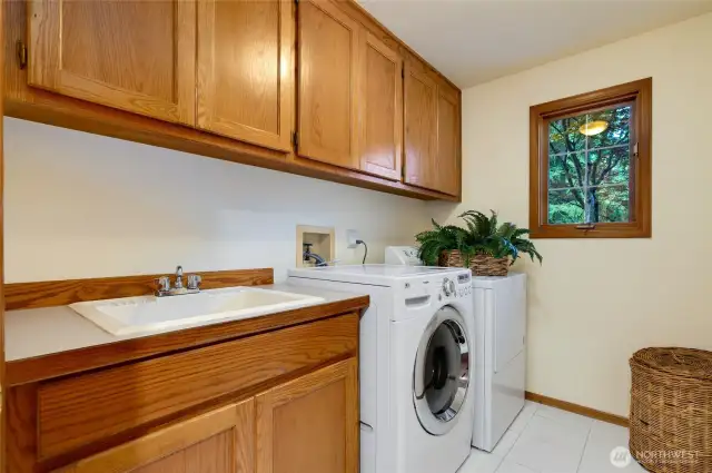 Well-appointed laundry room on the main floor with ample cabinetry, utility sink, and full-size washer and dryer that stay.