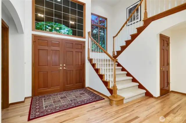 Step into a grand two-story foyer featuring elegant hardwood floors, a sweeping staircase, and striking double entry doors. Expansive windows fill the space with natural light, creating a warm and welcoming first impression.