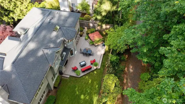 Aerial view reveals a beautifully maintained home with a spacious deck, lush lawn, and direct access to a scenic greenbelt trail. Surrounded by mature trees, this private outdoor oasis is ideal for peaceful living and effortless entertainment.