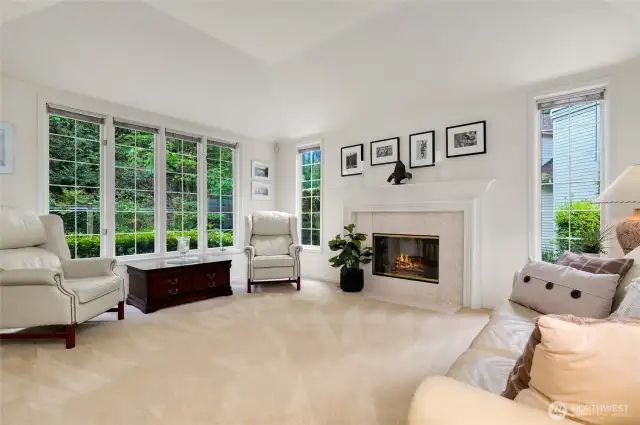 Bright and inviting formal living room with soaring ceilings, a cozy gas fireplace, and expansive picture windows. A space perfect for entertaining or relaxing in natural light.