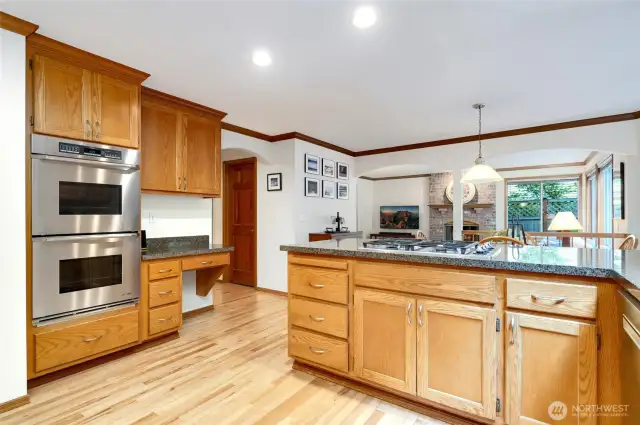 Another look at the spacious kitchen with granite countertops, double oven, built-in desk, and gas cooktop—perfect for cooking and gathering. Opens to a cozy family room with a gas fireplace for seamless everyday living.
