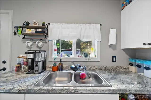 Kitchen window above the sink looks out back of home and yard space