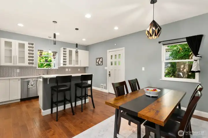 Bright, open-concept kitchen and dining area with stylish pendant lighting, gleaming hardwood floors, and sleek white cabinetry.