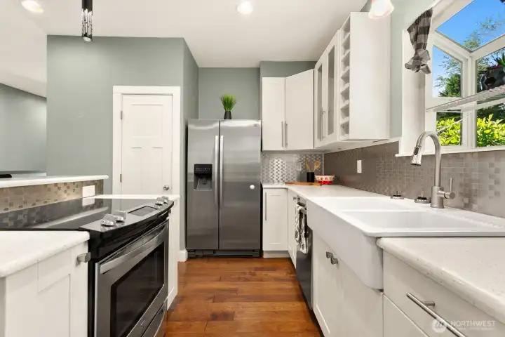 Chef-inspired kitchen featuring large countertops, a deep farmhouse sink, stainless steel appliances, and sunny garden views from the window above.