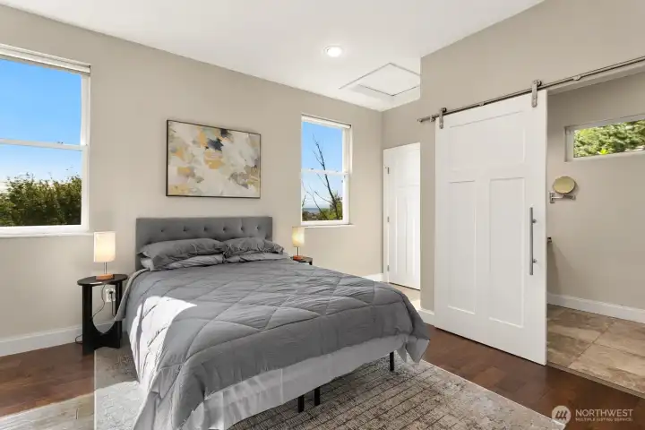 Wake up to natural light and calming views in this serene primary suite, complete with warm wood floors, a modern barn door, and private en suite access.