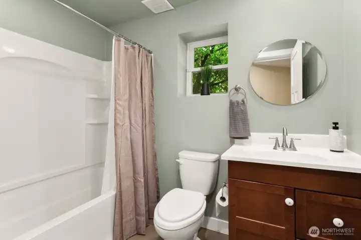 This bright and inviting downstairs bathroom features a full tub and shower, modern fixtures, tile floor, and a window for natural light.