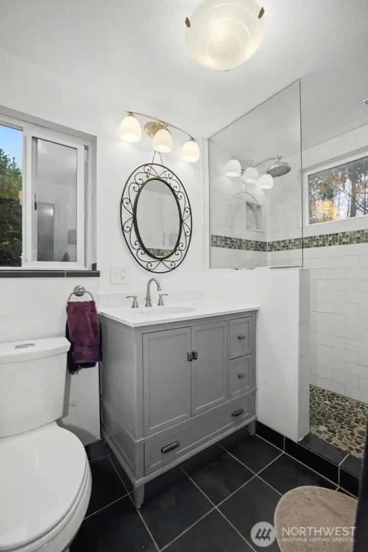 A handsome three-quarter primary bath boasts of custom tile and vintage look vanity.