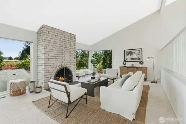 Light-filled living room with masonry fireplace, walls of windows & vaulted ceilings