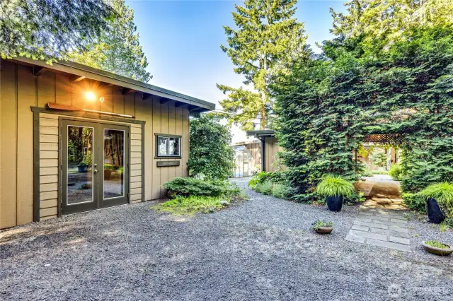 Front access to the home through the paved breezeway at the right. At left is an outbuilding. Use as a shop or hobby space?